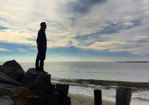 a man stands on rocks overlooking the beach by fort moultrie on sullivan's island, south carolina, photographed by jamie bannon photography.