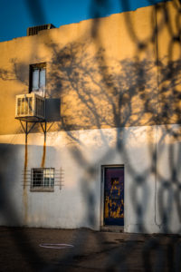 golden hour sun setting on a yellow and white building through a chain link fence in denver, colorado, photographed by jamie bannon photography.