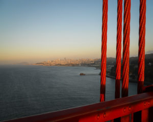 sunset viewed with the giant red cables of the golden gate bridge in the foreground, photographed by jamie bannon photography.
