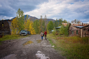 a young couple walks down the dirt road in mccarthy, alaska, photographed by jamie bannon photography.