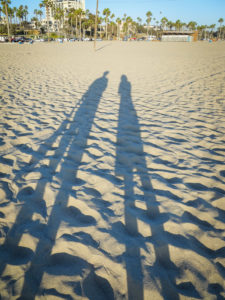 long shadows of a man and a woman on the beach in santa monica, california, photographed by jamie bannon photography.