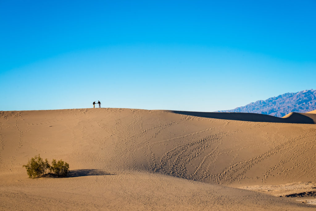 two hikers meet on top of a sand dune in death valley, california, photographed by jamie bannon photography.