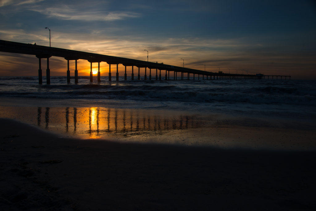 the sun sets over the ocean beach boardwalk in san diego, california, photographed by jamie bannon photography.