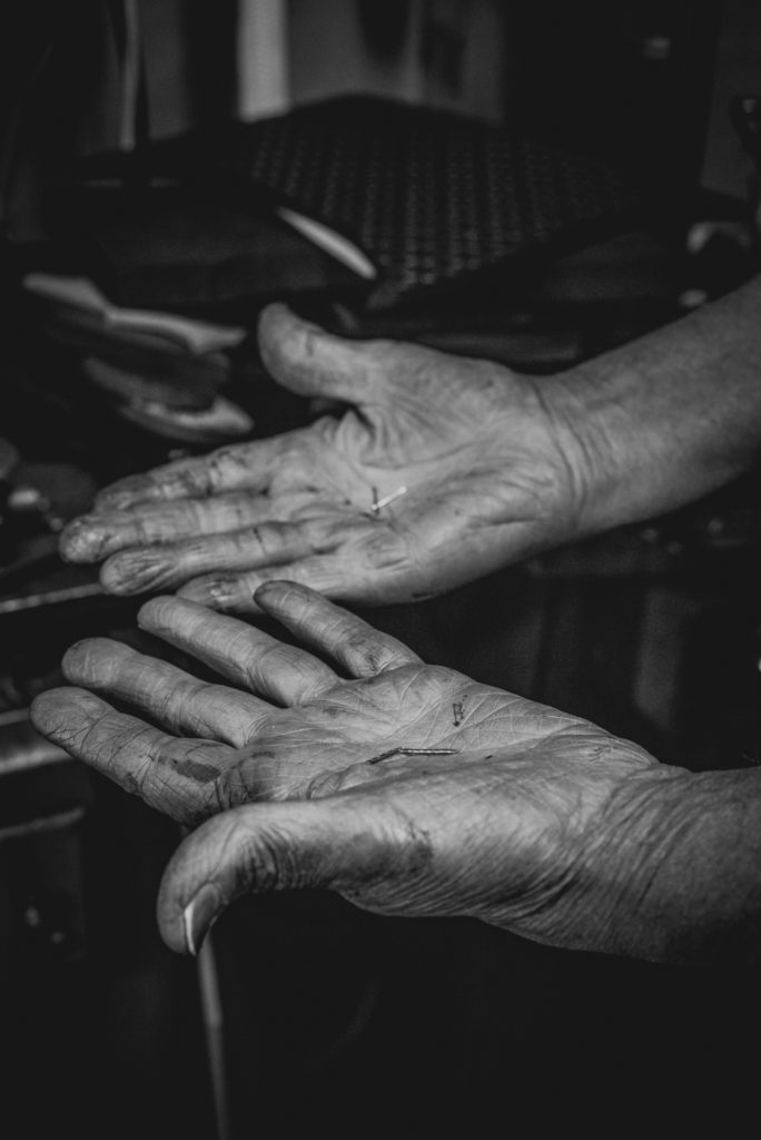 a cobbler's hands holding shoe nails in his shop in unionville, connecticut, photographed by jamie bannon photography.