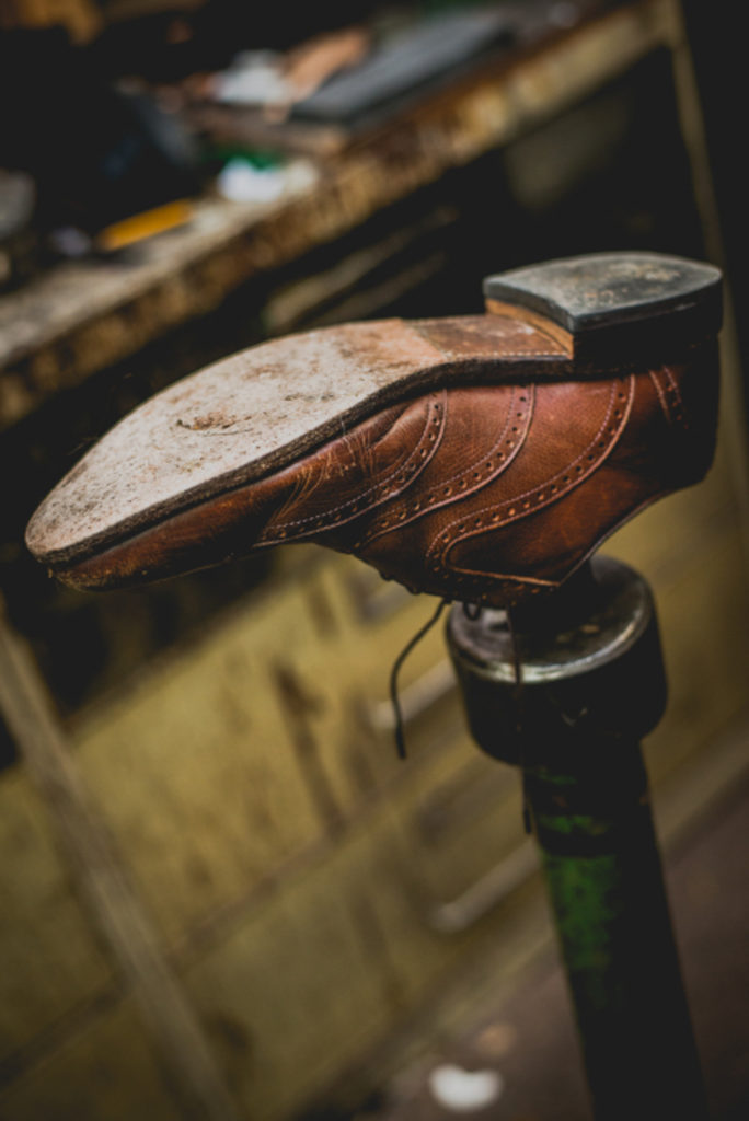 detail of a brown leather shoe on a stand to be repaired at a cobbler shop in unionville, connecticut, photographed by jamie bannon photography.
