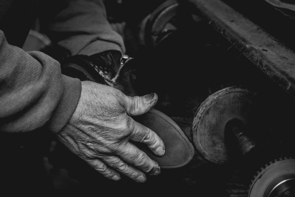 black and white close-up of a cobbler's hands working in his shoe repair shop in unionville, connecticut, photographed by jamie bannon photography.
