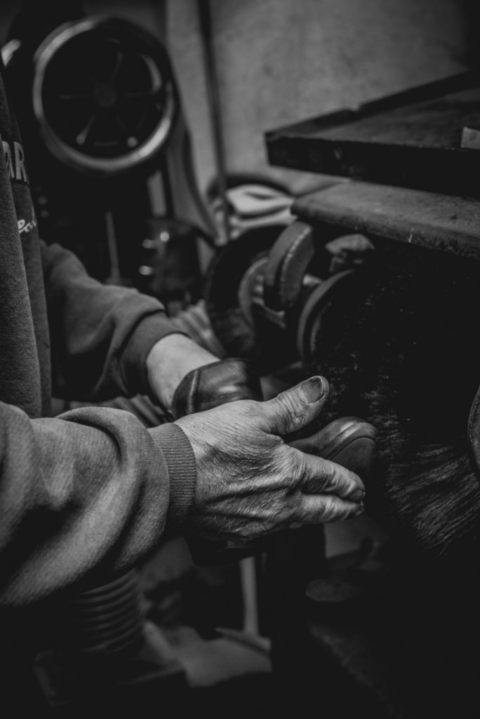 black and white close-up of a cobbler's hands working in his shoe repair shop in unionville, connecticut, photographed by jamie bannon photography.