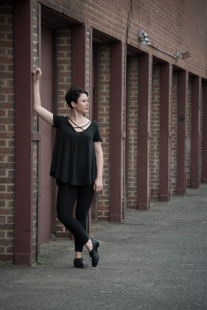 a tap dancer poses outside in front of a row of garages, in west hartford, connecticut, photographed by jamie bannon photography.