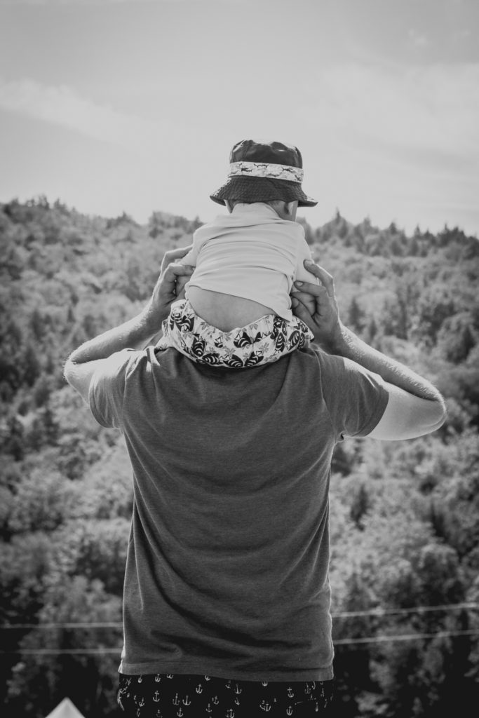black and white image of a small boy riding on his dad's shoulders outdoors in vermont, photographed by jamie bannon photography.