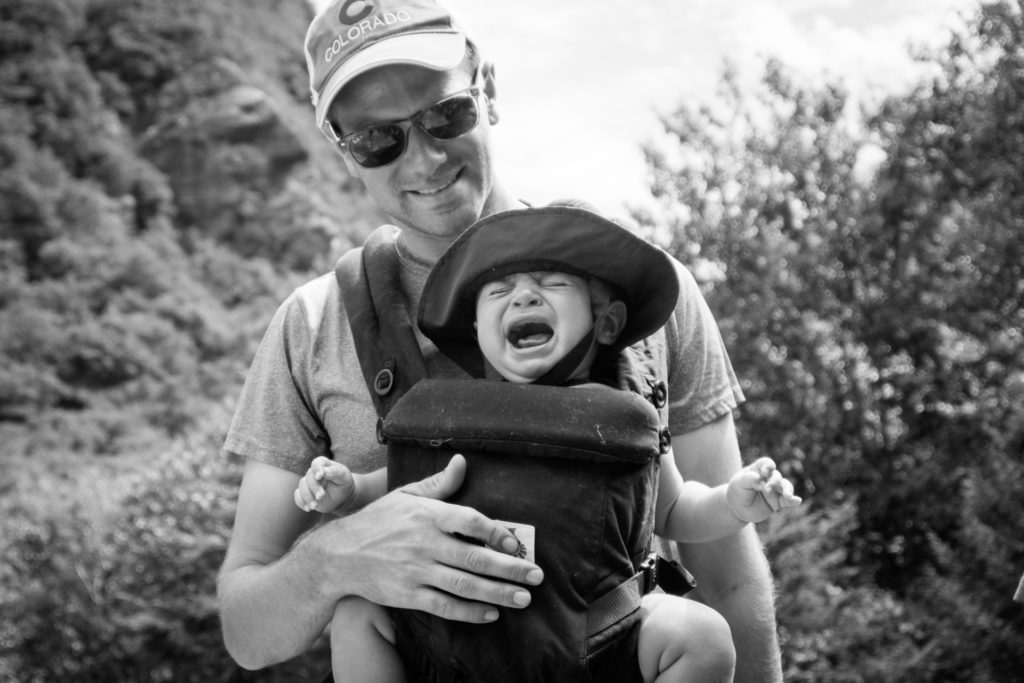 black and white portrait of a dad laughing while his son cries on a hike at smugglers' notch state park in vermont, photographed by jamie bannon photography.