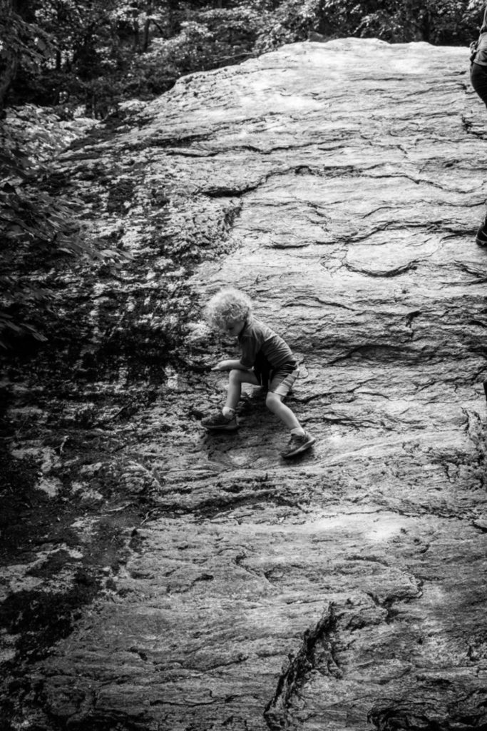 a small boy climbs up a boulder at smugglers' notch state park in vermont, photographed by jamie bannon photography.