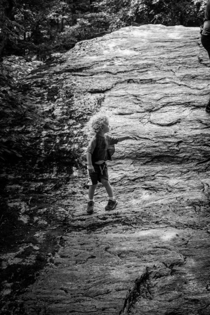a small boy climbs up a boulder at smugglers' notch state park in vermont, photographed by jamie bannon photography.