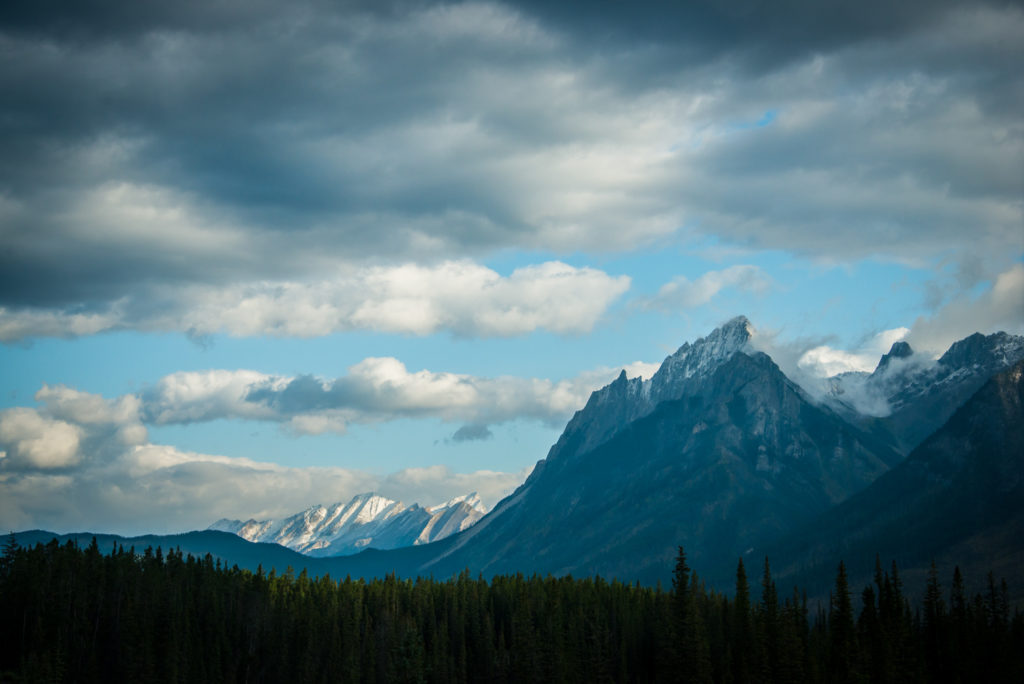 jagged rocky mountains in sunlight with clouds on the icefields parkway through banff and jasper national parks in alberta, canada, photographed by jamie bannon photography.