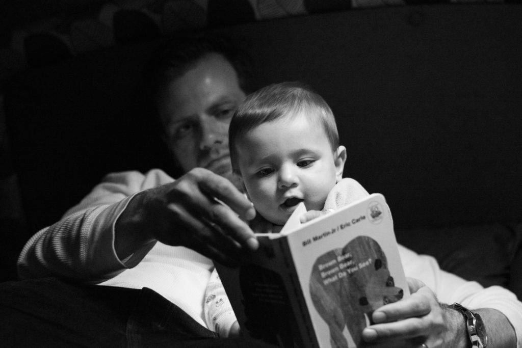 black and white picture of a dad reading to his baby in a camper van in banff, alberta, canada, photographed by jamie bannon photography.