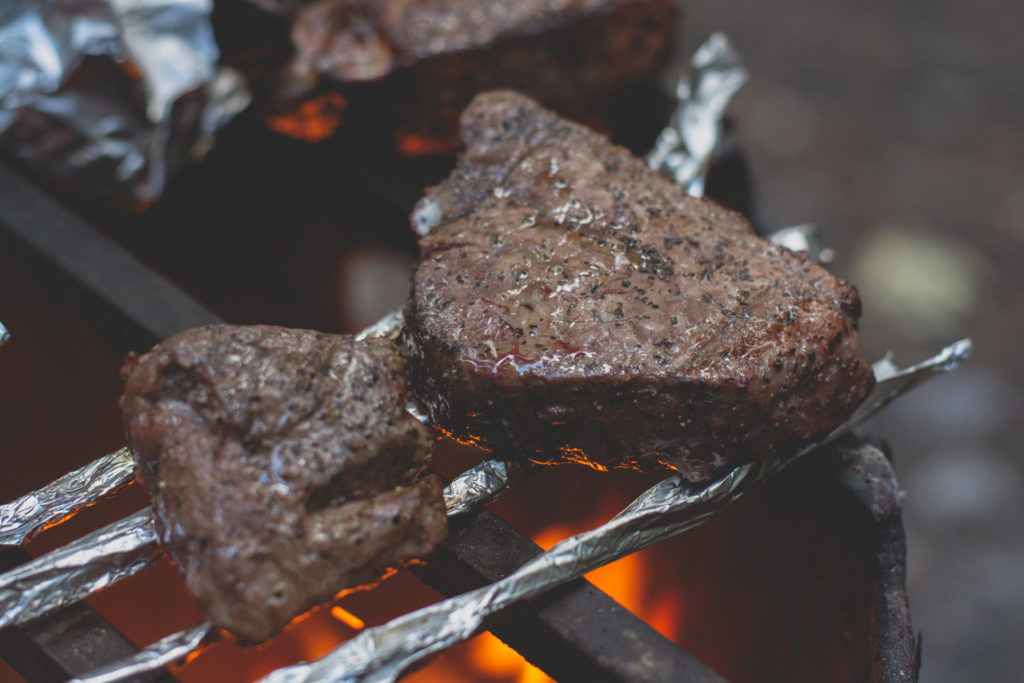 steaks cooking on an open campfire in british columbia, canada, photographed by jamie bannon photography.
