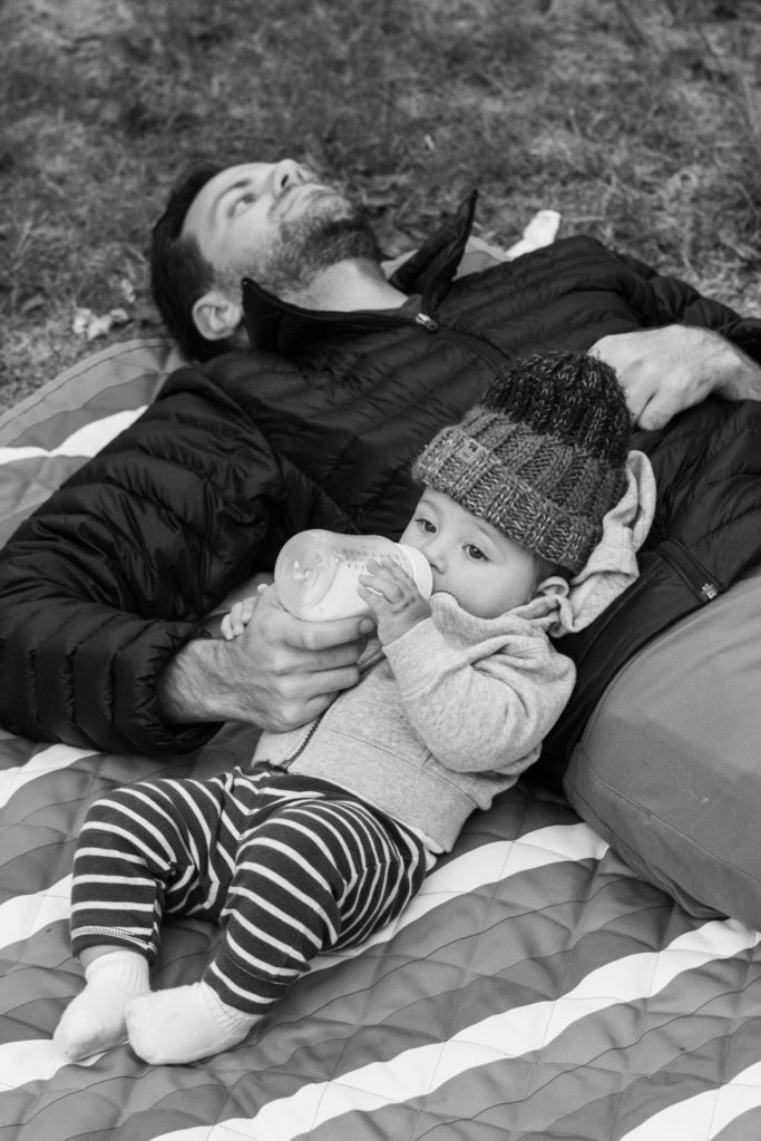 black and white picture of a dad feeding his baby at a campsite on the olympic peninsula, washington, photographed by jamie bannon photography.