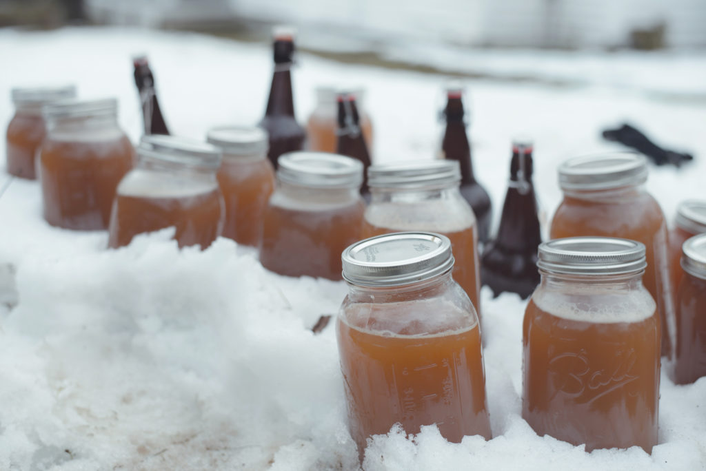 growlers and jars of freshly made apple cider chill in the snow outside on a cold new england winter day in connecticut, photographed by jamie bannon photography.