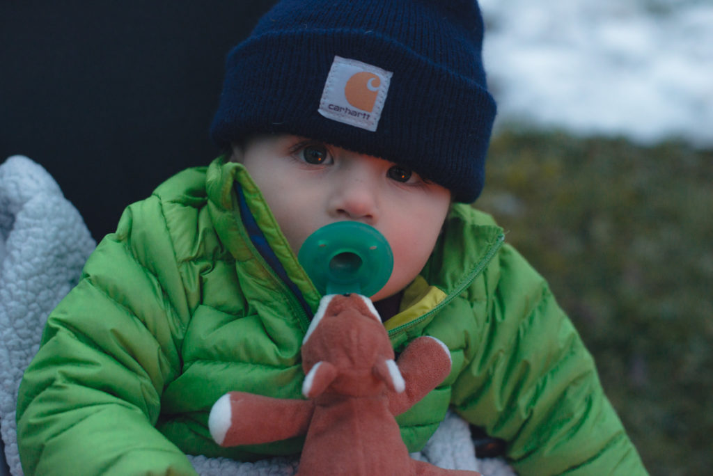 a baby sits bundled up by the fire outdoors on a cold new england winter day, photographed by jamie bannon photography.