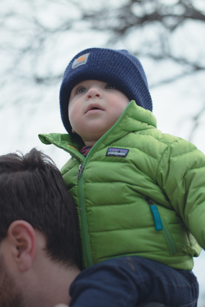 a baby boy rides on his dad's shoulders, bundled up in his patagonia jacket and carhartt hat on a cold new england winter day, photographed by jamie bannon photography.