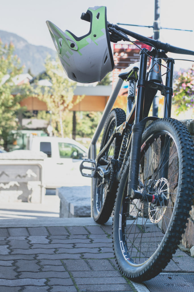 a helmet hangs on a mountain bike handlebar at whistler in british columbia, canada, photographed by jamie bannon photography.