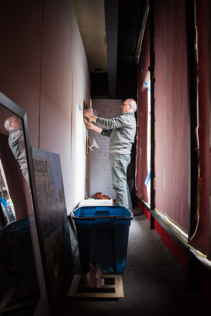 a gallery owner installs artwork in an empty storefront window in downtown hartford, connecticut, photographed by jamie bannon photography.