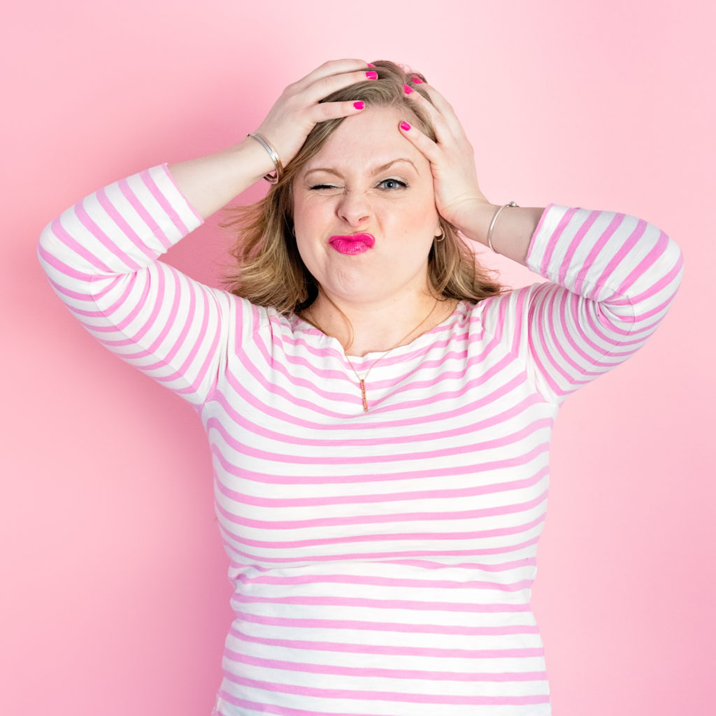 portrait of a female entrepreneur making a funny face in front of a pink backdrop in a pink and white striped shirt, as part of a personal branding shoot by jamie bannon photography.