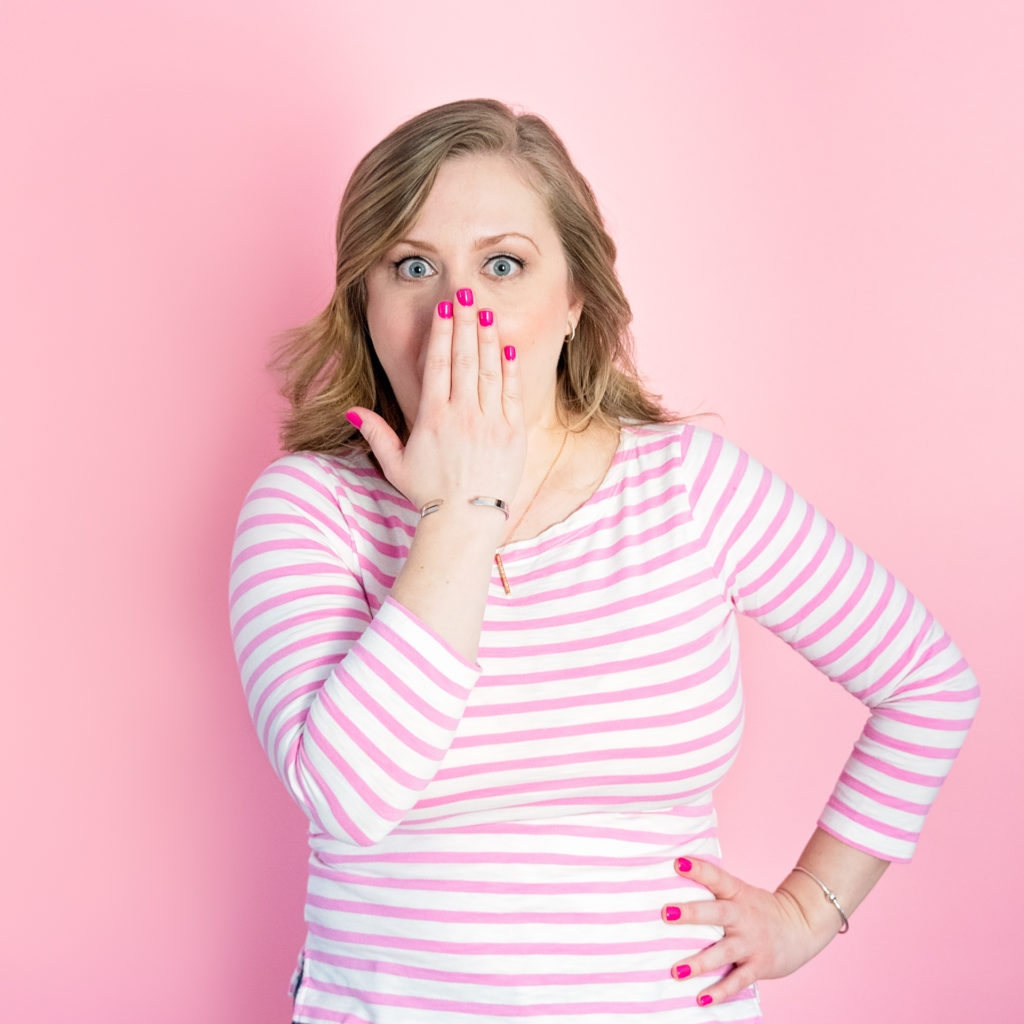portrait of a female entrepreneur making a funny face in front of a pink backdrop in a pink and white striped shirt, as part of a personal branding shoot by jamie bannon photography.